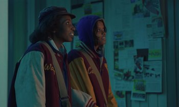 Movie still from “The Silent Twins” (2022), directed by Agnieszka Smoczynska – A couple of young men standing next to each other in a room; Medium shot, Low angle