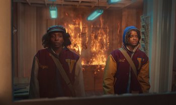 Movie still from “The Silent Twins” (2022), directed by Agnieszka Smoczynska – A couple of people that are standing in front of a fire; Medium shot, High angle