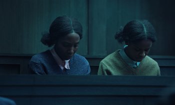 Movie still from “The Silent Twins” (2022), directed by Agnieszka Smoczynska – Two young women sitting in front of each other; Medium shot, High angle