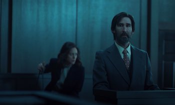 Movie still from “The Silent Twins” (2022), directed by Agnieszka Smoczynska – A man and a woman in a suit and tie in a room; Medium shot, Low angle