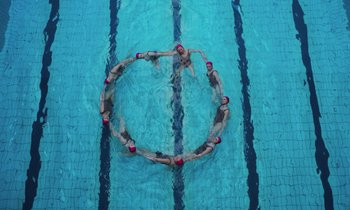 Movie still from “The Silent Twins” (2022), directed by Agnieszka Smoczynska – A group of people in a swimming pool doing different things; Extreme Wide shot, Overhead angle