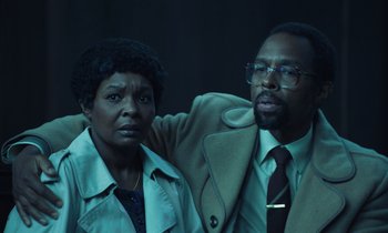 Movie still from “The Silent Twins” (2022), directed by Agnieszka Smoczynska – A man and a woman posing for a picture; Medium shot, Low angle