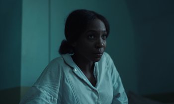 Movie still from “The Silent Twins” (2022), directed by Agnieszka Smoczynska – A woman in a white shirt is looking at the camera; Close Up shot, High angle