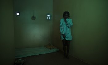 Movie still from “The Silent Twins” (2022), directed by Agnieszka Smoczynska – A person standing in a room with a cell phone to their ear; Medium shot, High angle