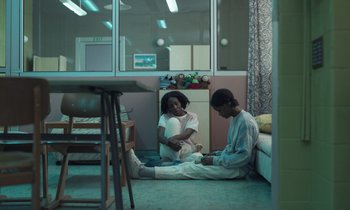 Movie still from “The Silent Twins” (2022), directed by Agnieszka Smoczynska – A man and a woman sitting on the floor in a room; Wide shot, High angle