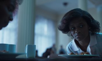 Movie still from “The Silent Twins” (2022), directed by Agnieszka Smoczynska – A woman sitting in front of a plate of food and a coffee mug; Close Up shot, Over the shoulder angle