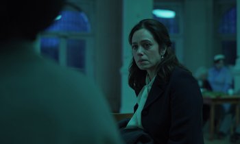 Movie still from “The Silent Twins” (2022), directed by Agnieszka Smoczynska – A woman sitting in front of a man in front of a window; Medium shot, Over the shoulder angle