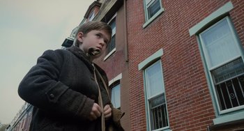 Movie still from “The Sixth Sense” (1999), directed by M. Night Shyamalan – A young boy standing in front of a brick building; Medium shot, Low angle