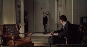 Movie still from “The Sixth Sense” (1999), directed by M. Night Shyamalan – A man in a suit and tie standing in front of a door; Wide shot, High angle