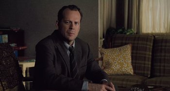 Movie still from “The Sixth Sense” (1999), directed by M. Night Shyamalan – A man in a suit sitting in front of a couch; Medium shot, Low angle