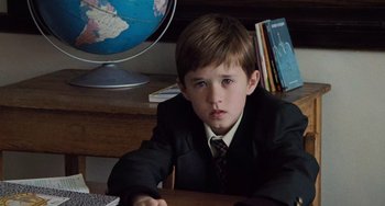 Movie still from “The Sixth Sense” (1999), directed by M. Night Shyamalan – A boy in a suit and tie sitting at a desk; Close Up shot, High angle