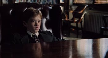 Movie still from “The Sixth Sense” (1999), directed by M. Night Shyamalan – A boy in a suit sitting at a table in a room; Medium shot, High angle