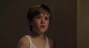Movie still from “The Sixth Sense” (1999), directed by M. Night Shyamalan – A young boy in a white tank top looking at the camera; Close Up shot, High angle