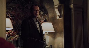 Movie still from “The Sixth Sense” (1999), directed by M. Night Shyamalan – A man in a suit standing in front of a lamp in a dimly - lit room; Medium shot, Low angle