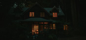 Movie still from “The Sky Is Everywhere” (2022), directed by Josephine Decker – People sitting on the steps of a house lit up at night; Extreme Wide shot, Low angle