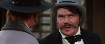 Movie still from “The Specialists” (1969), directed by Sergio Corbucci – A man in a top hat and a mustache talking to another man in a suit; Close Up shot, Over the shoulder angle