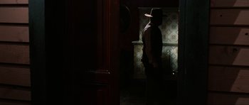 Movie still from “The Specialists” (1969), directed by Sergio Corbucci – A man standing in a dark room wearing a hat; Wide shot, Over the shoulder angle