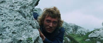 Movie still from “The Specialists” (1969), directed by Sergio Corbucci – A man with long blonde hair climbing on a rock wall; Close Up shot, Low angle