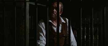 Movie still from “The Specialists” (1969), directed by Sergio Corbucci – A man with a beard is sitting behind bars; Medium shot, Low angle