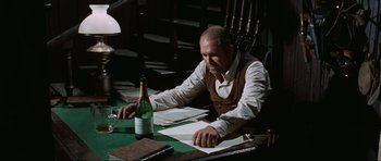 Movie still from “The Specialists” (1969), directed by Sergio Corbucci – A man sitting at a table in front of a bottle of wine; Medium shot, High angle