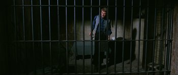 Movie still from “The Specialists” (1969), directed by Sergio Corbucci – A man standing in a jail cell behind bars; Wide shot, High angle