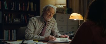 Movie still from “The Starling” (2021), directed by Theodore Melfi – An older man sitting at a desk looking at a book; Medium shot, Over the shoulder angle