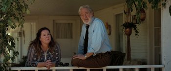 Movie still from “The Starling” (2021), directed by Theodore Melfi – An older man sitting on a railing next to a woman; Medium shot, Over the shoulder angle