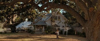 Movie still from “The Starling” (2021), directed by Theodore Melfi – A person standing in front of a house under a large tree; Extreme Wide shot, Low angle