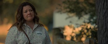 Movie still from “The Starling” (2021), directed by Theodore Melfi – A woman wearing a visitor badge stands in front of trees; Medium shot, Over the shoulder angle