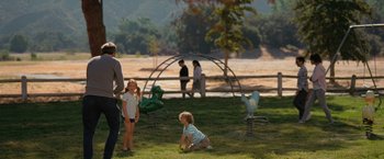 Movie still from “The Starling” (2021), directed by Theodore Melfi – A group of people in a field with a playground in the background; Wide shot, Over the shoulder angle