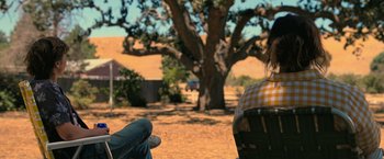 Movie still from “The Starling” (2021), directed by Theodore Melfi – A person sitting on a chair in front of a tree; Medium shot, Over the shoulder angle