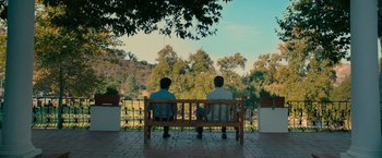 Movie still from “The Starling” (2021), directed by Theodore Melfi – Two men sitting on a bench looking out on a sunny day; Extreme Wide shot, High angle