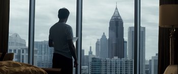 Movie still from “Due Date” (2010), directed by Todd Phillips – A man standing in front of a window looking out at a city skyline; Wide shot, Over the shoulder angle
