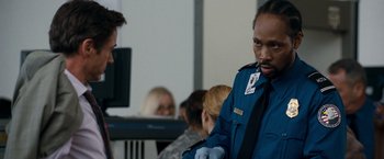 Movie still from “Due Date” (2010), directed by Todd Phillips – A man in a blue uniform standing in front of a group of people; Close Up shot, Over the shoulder angle