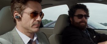 Movie still from “Due Date” (2010), directed by Todd Phillips – A man in a suit and sunglasses in the back of a car; Close Up shot, Over the shoulder angle