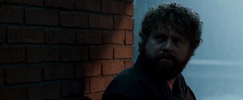 Movie still from “Due Date” (2010), directed by Todd Phillips – A man with curly hair and a beard is sitting against a brick wall; Close Up shot, Over the shoulder angle
