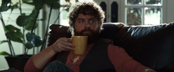 Movie still from “Due Date” (2010), directed by Todd Phillips – A man sitting on a couch holding a cup of coffee; Medium shot, Over the shoulder angle