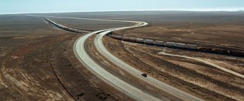 Movie still from “Due Date” (2010), directed by Todd Phillips – An aerial view of a highway with a train on the tracks; Extreme Wide shot, High angle