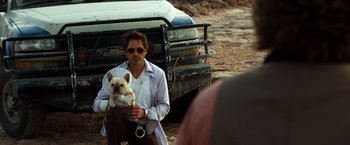 Movie still from “Due Date” (2010), directed by Todd Phillips – A man holding a dog in front of a truck; Medium shot, Over the shoulder angle