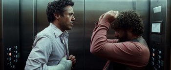 Movie still from “Due Date” (2010), directed by Todd Phillips – Two men in an elevator , one of which has his arm wrapped around his shoulder; Medium shot, Over the shoulder angle