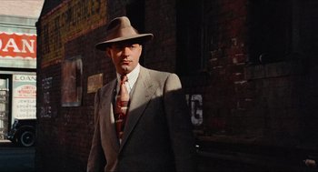 Movie still from “The Sting” (1973), directed by George Roy Hill – A man in a suit and hat standing in front of a brick building; Medium shot, Low angle