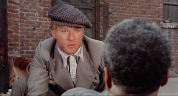 Movie still from “The Sting” (1973), directed by George Roy Hill – A man in a suit and a hat talking to another man in front of a brick wall; Close Up shot, Over the shoulder angle