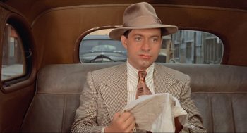 Movie still from “The Sting” (1973), directed by George Roy Hill – A man sitting in the back seat of a car holding a newspaper; Close Up shot, Over the shoulder angle