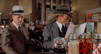 Movie still from “The Sting” (1973), directed by George Roy Hill – A man in a suit and hat reading a newspaper; Medium shot, Over the shoulder angle