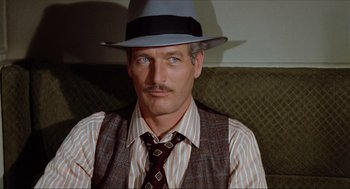 Movie still from “The Sting” (1973), directed by George Roy Hill – A man in a hat and a tie sitting on a couch; Close Up shot, Over the shoulder angle
