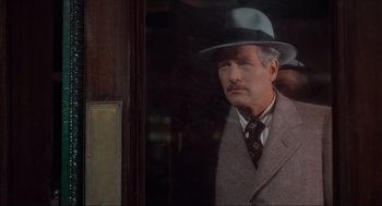 Movie still from “The Sting” (1973), directed by George Roy Hill – A man wearing a suit and a hat standing in front of a window; Close Up shot, Over the shoulder angle