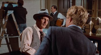 Movie still from “The Sting” (1973), directed by George Roy Hill – A man wearing a hat talking to another man in a suit; Medium shot, Over the shoulder angle