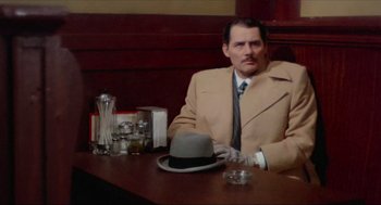 Movie still from “The Sting” (1973), directed by George Roy Hill – A man sitting at a table with a hat; Medium shot, High angle