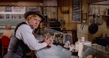 Movie still from “The Sting” (1973), directed by George Roy Hill – A man sitting at a counter in front of a bar; Medium shot, Over the shoulder angle