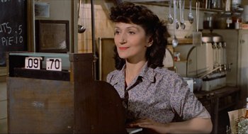 Movie still from “The Sting” (1973), directed by George Roy Hill – A woman sitting at a table in front of a stove; Medium shot, Over the shoulder angle